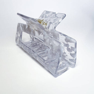 A rectangular, clear marbled plastic hair clip with a visible metal spring is angled on a white background.